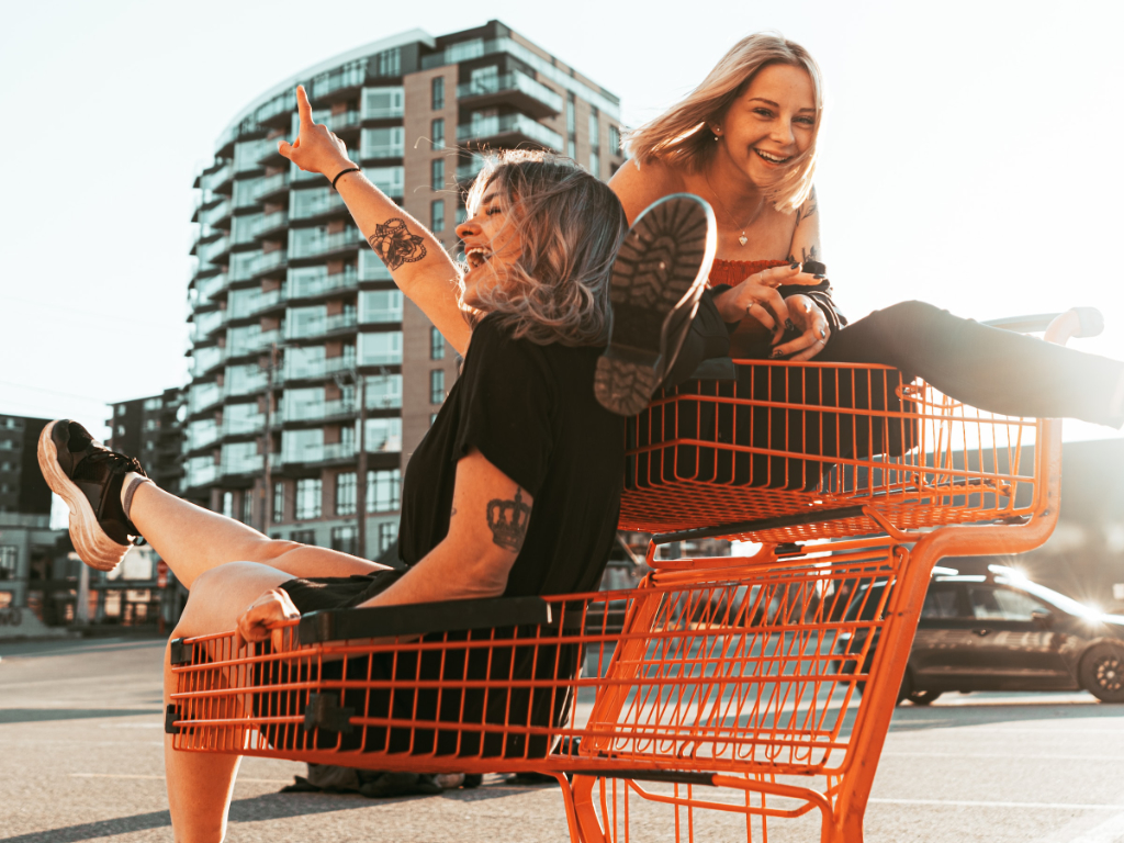 Zwei Frauen sitzen lachend im leeren Einkaufswagen