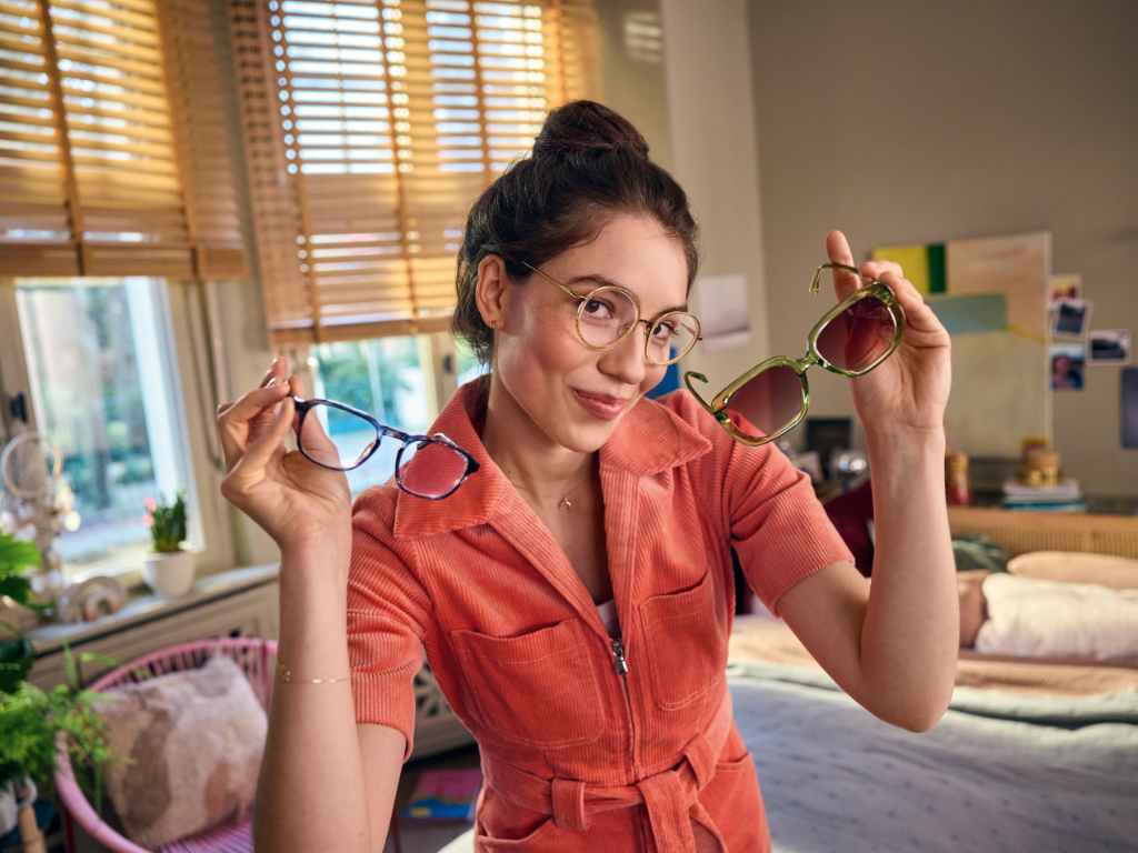 Brillenträgerin hält Brille und Sonnenbrille hoch zu Apllo Plus-Brillenmietkonzept