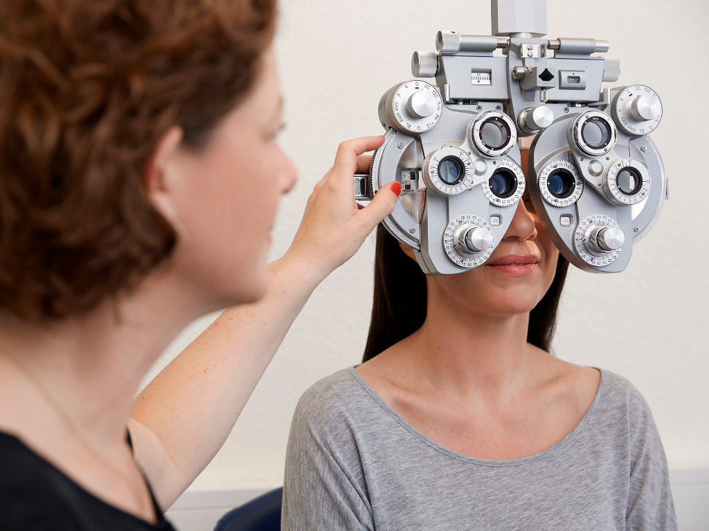 Eine Augenoptikerin führt mittels Phoropter einen Sehtest bei einer Kundin durch