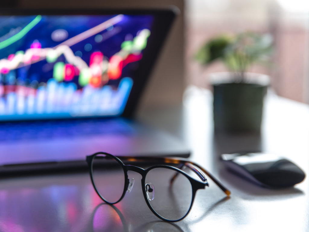 Laptop aufgeklappt mit Grafiken, eine Brille liegt davor auf dem Tisch