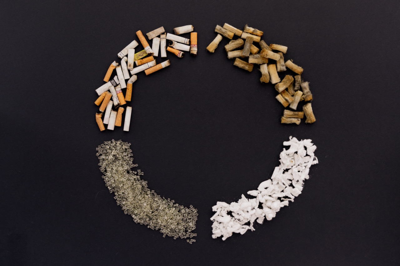 Kreisförmig angeordnete Materialien auf dunklem Hintergrund – Zigarettenreste, Fasern und Kunststoffgranulat als Symbol für Recycling und Upcycling.