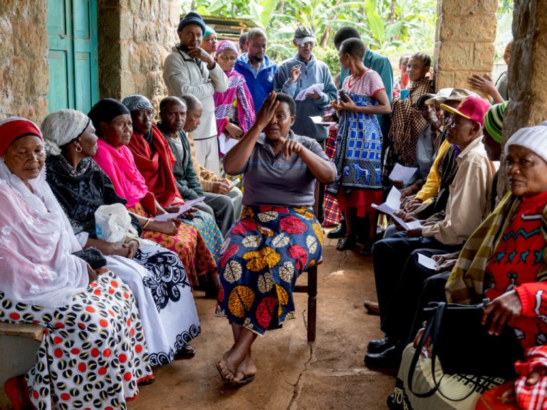 Gruppe von Menschen in Afrika in einem überdachten Außenbereich, eine Person in der Mitte probiert eine Brille an