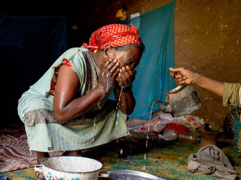 Frau in Afrika wäscht sich die Augen mit Wasser