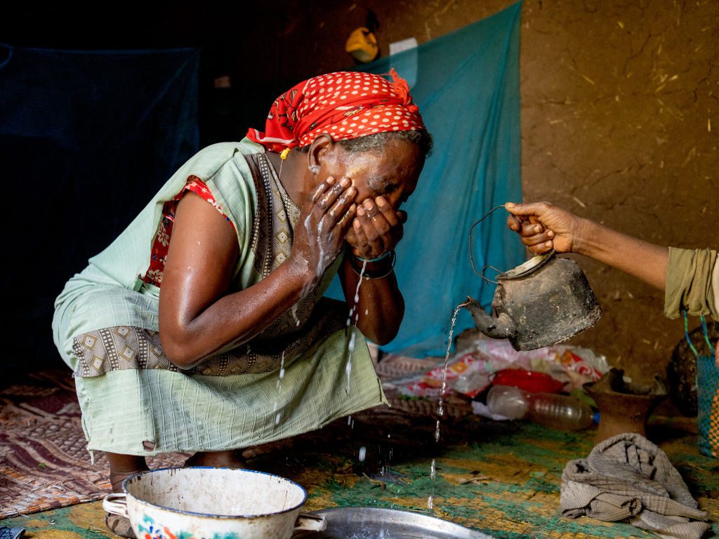 Frau in Afrika wäscht sich die Augen mit Wasser