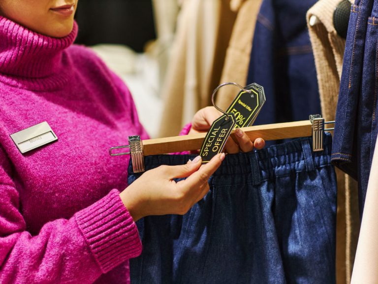 Nahaufnahme einer Frau, die Verkaufsetiketten an Kleidungsstücken in einer Boutique anbringt