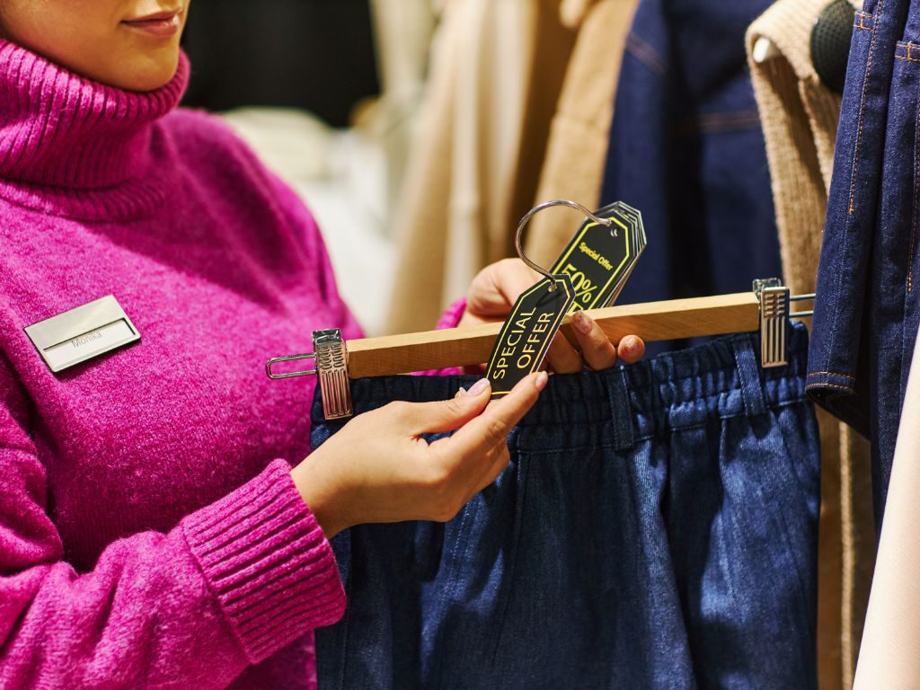 Nahaufnahme einer Frau, die Verkaufsetiketten an Kleidungsstücken in einer Boutique anbringt