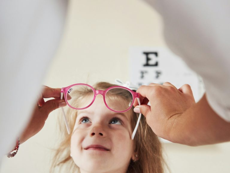 Mädchen bekommt Brille von einem Optiker aufgesetzt