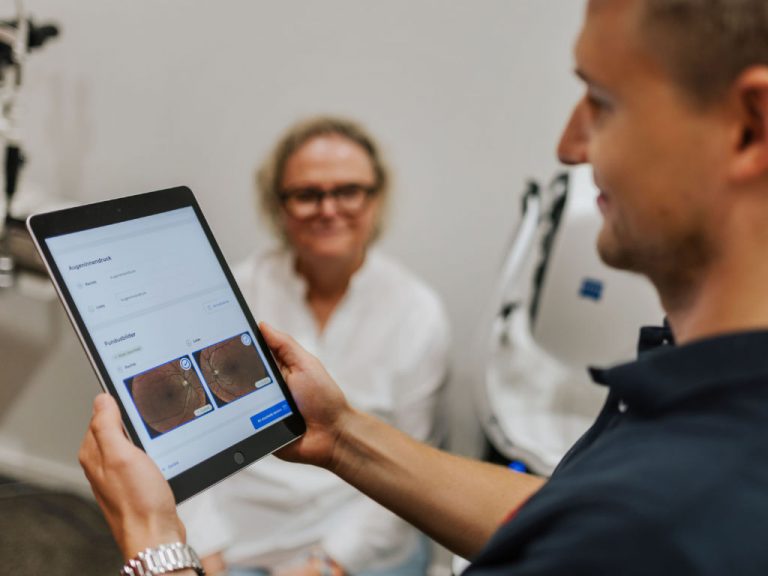 Mann hält Tablet in Händen bei Augenvorsorgeuntersuchung