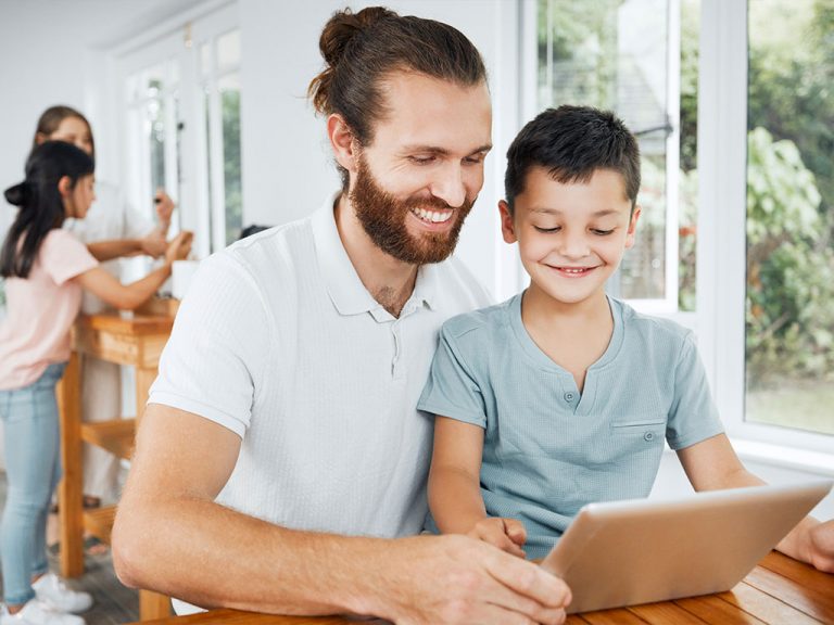 Vater und Sohn lächeln, während sie gemeinsam auf ein Tablet schauen