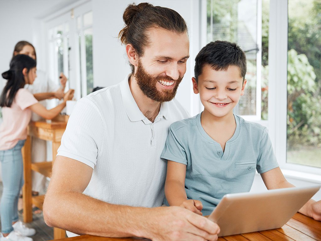 Vater und Sohn lächeln, während sie gemeinsam auf ein Tablet schauen