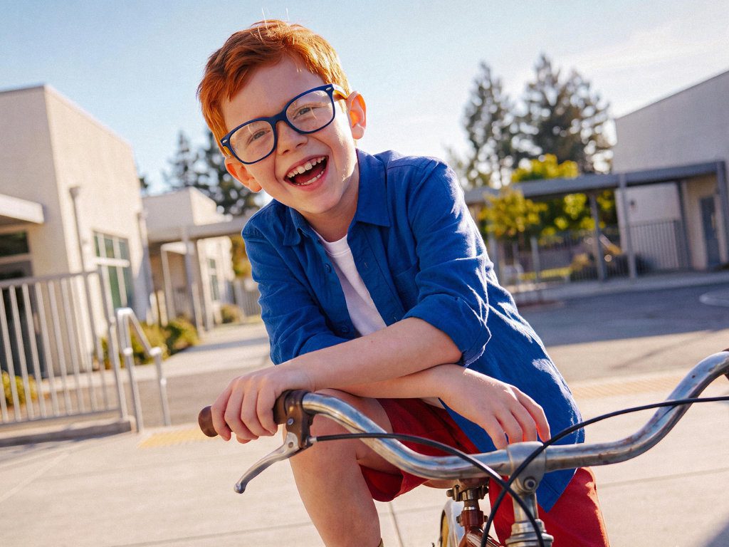Junge auf Fahrrad trägt Brille und lacht in die Kamera