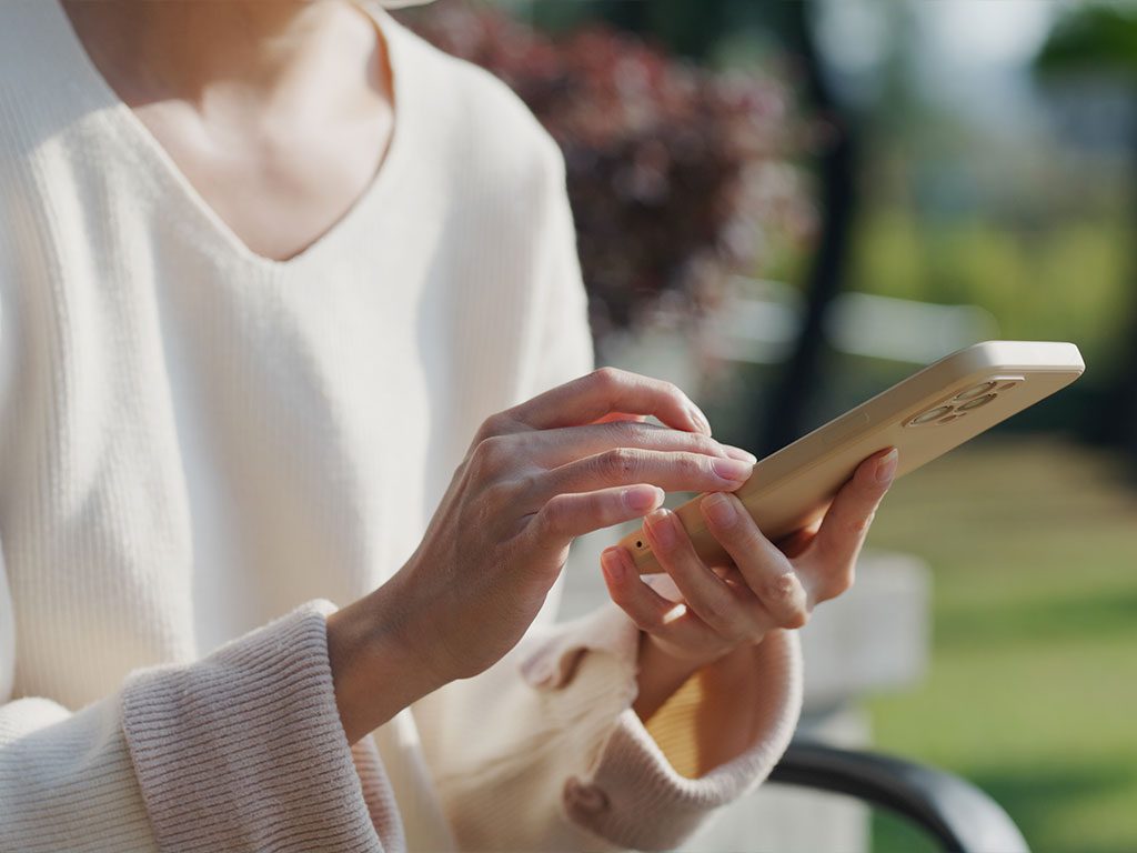 Eine Person bedient im Freien ein Smartphone mit beiden Händen.