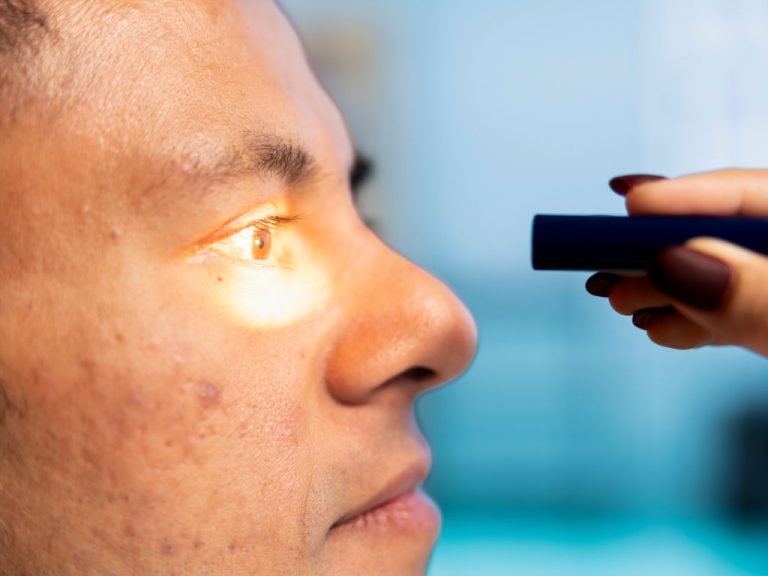 Optometrist leuchtet einem Mann bei Sehtest ins Auge