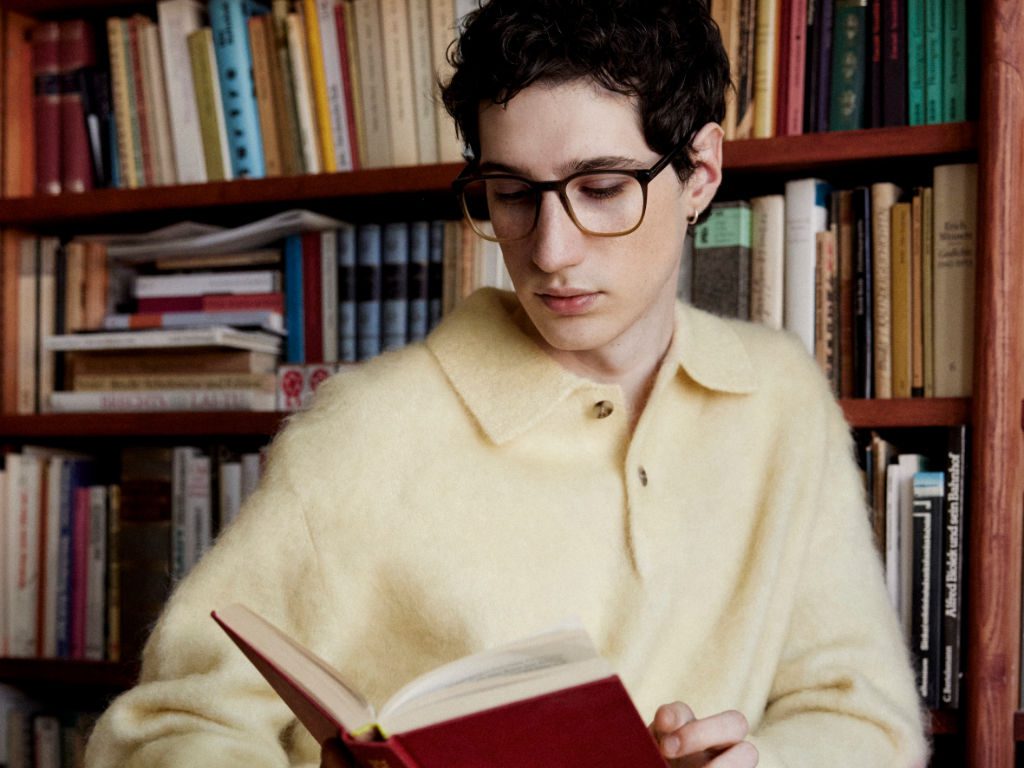 Männliches Model mit Brille in Bibliothek liest Buch