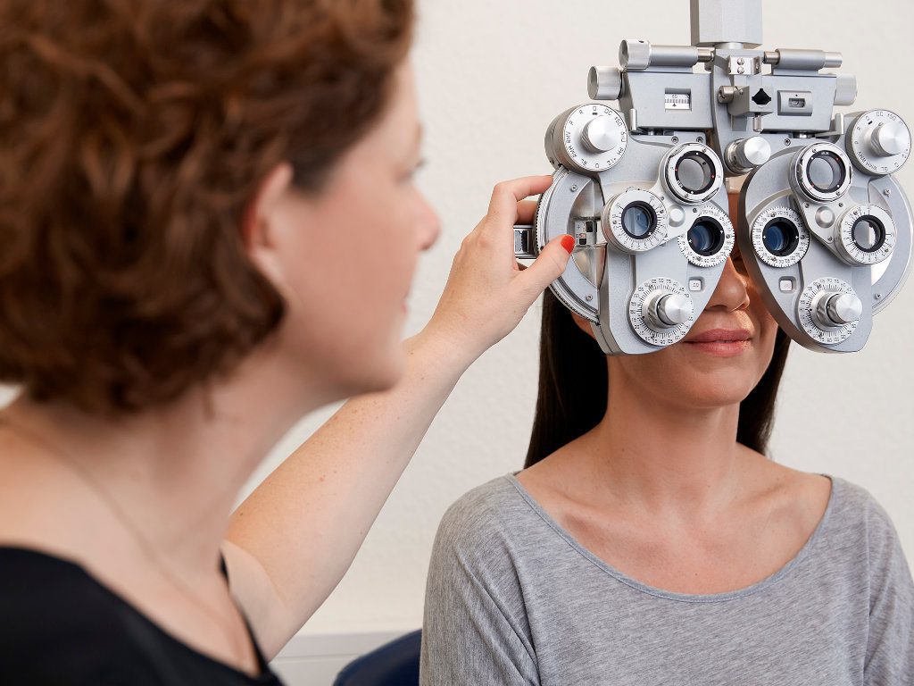 Augenoptikerin/Optometristin macht Sehtest am Phoropter bei einer Kundin