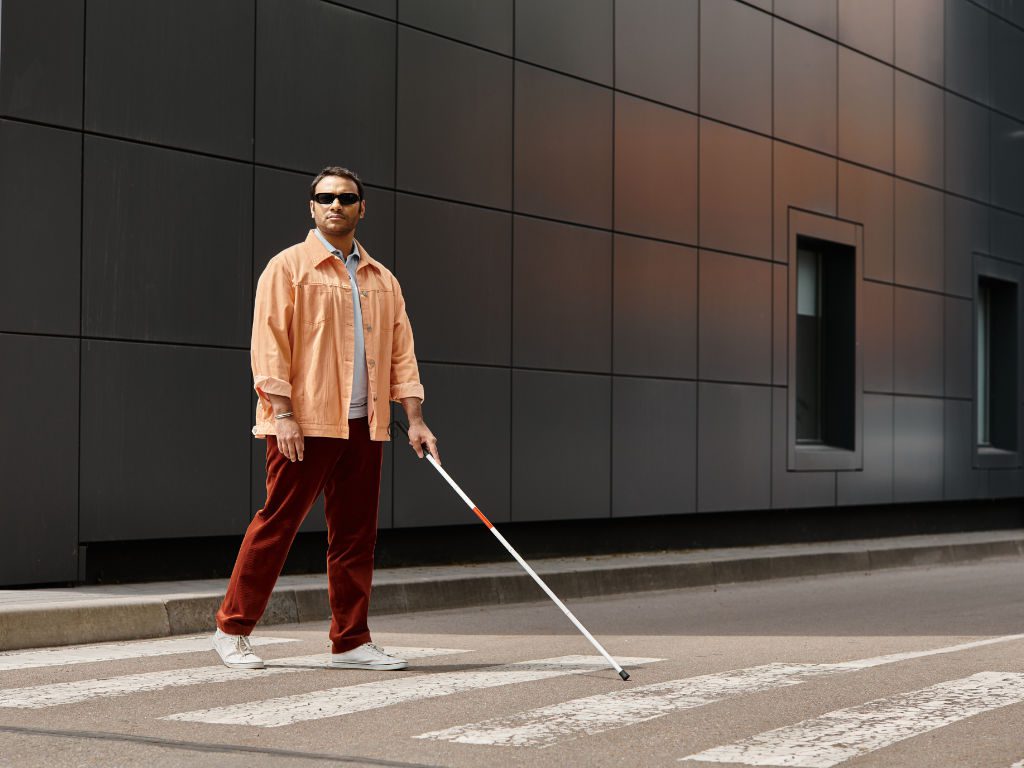 Mann mit Blindenstock überquert Fußgängerüberweg in der Stadt